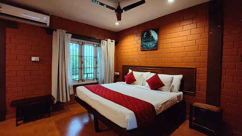 A double bed with open brick style wall behind the bed and a ceiling fan hanging from above inside the Executive Deluxe Rooms near Aliyar Dam at Ibex River Resort, Pollachi.