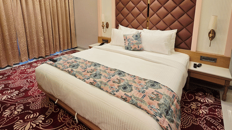 Elegant hotel bedroom with plush bed, patterned wall panel, warm lighting, and carpeted flooring.