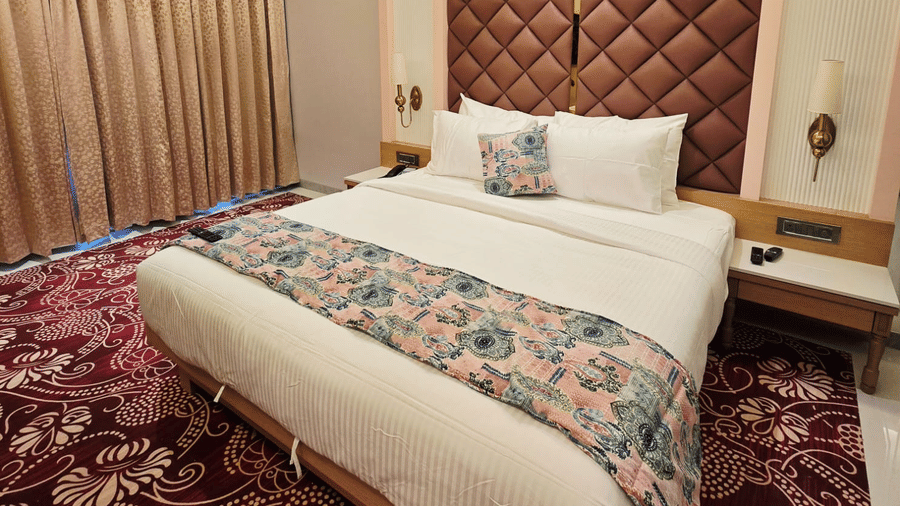 Elegant hotel bedroom with plush bed, patterned wall panel, warm lighting, and carpeted flooring.