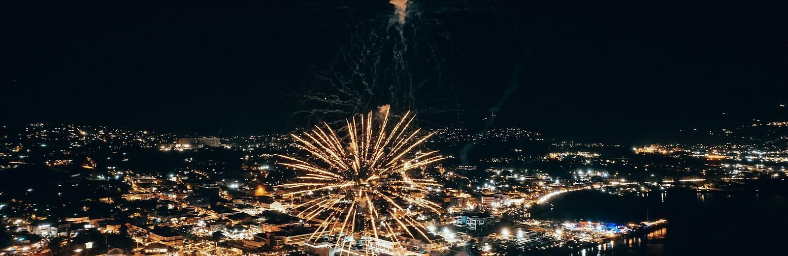 A firework bursts over a cityscape at night, illuminating the urban scene with a bright display.