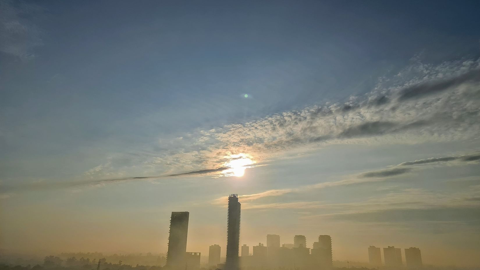 a far out view of Gurgaon with the sky line dotted with skyscrapers and the sun in the background.