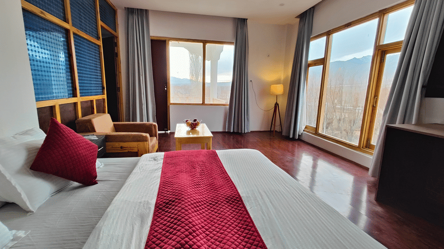 A bright, airy suite with a red bed runner and large windows overlooking the grounds at Indus Serenity Retreat.
