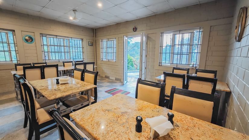 an image of seating arrangements inside a restaurant with a brown golden table and chairs - Ibex Stays & Trails, Valparai (Mistly)