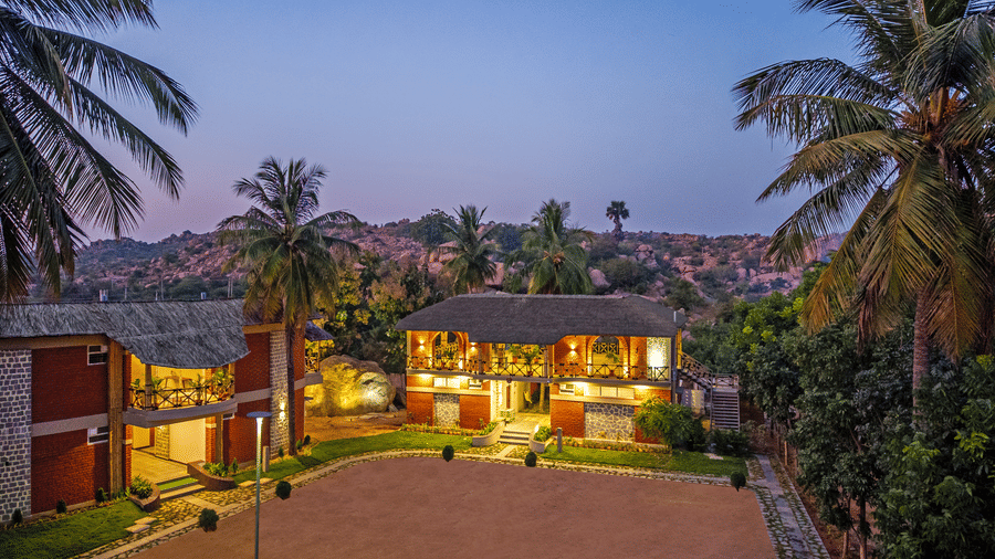 The resort buildings illuminated at dusk, showcasing the red-brick architecture and sandy courtyard - Nature Trails Ashoka Resort Hampi