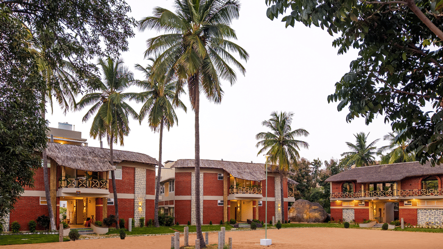 Resort exterior view looking across a dusty courtyard toward multi-story red-brick buildings and palm trees