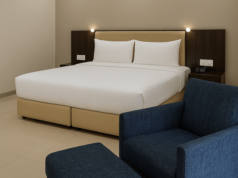 Superior Room at Tropicana Resort & Spa, Alibaug, featuring a large bed with crisp white linens and a tan base, positioned next to a plush navy blue armchair.