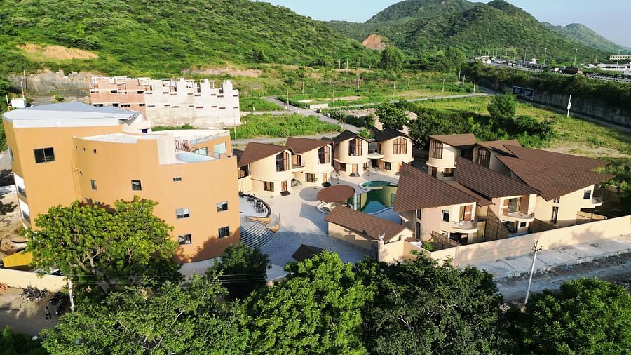 The Qualia Resort Club & Brewery, Udaipur nestled in a green, hilly landscape showcases multiple buildings with a consistent architectural style.