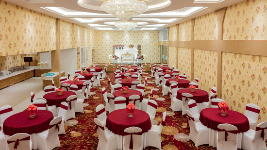 Wide view of banquet hall set up with round tables and red linen at Mango Grove Hotel.