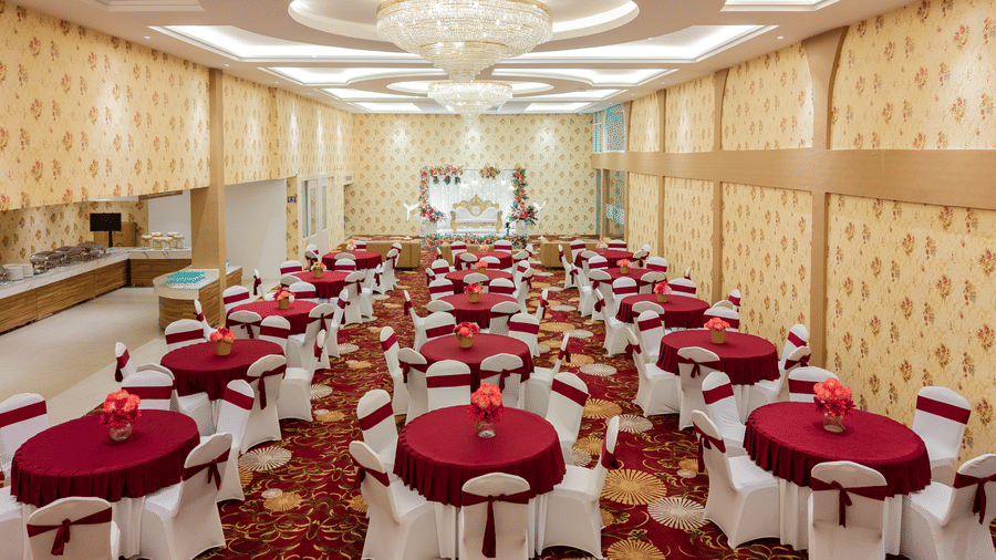 Wide view of banquet hall set up with round tables and red linen at Mango Grove Hotel.