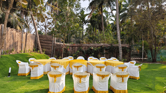 Tables and chairs arranged in the wedding lawn with trees in the backdrop at Ibex Resorts, Coimbatore (Kakarla).