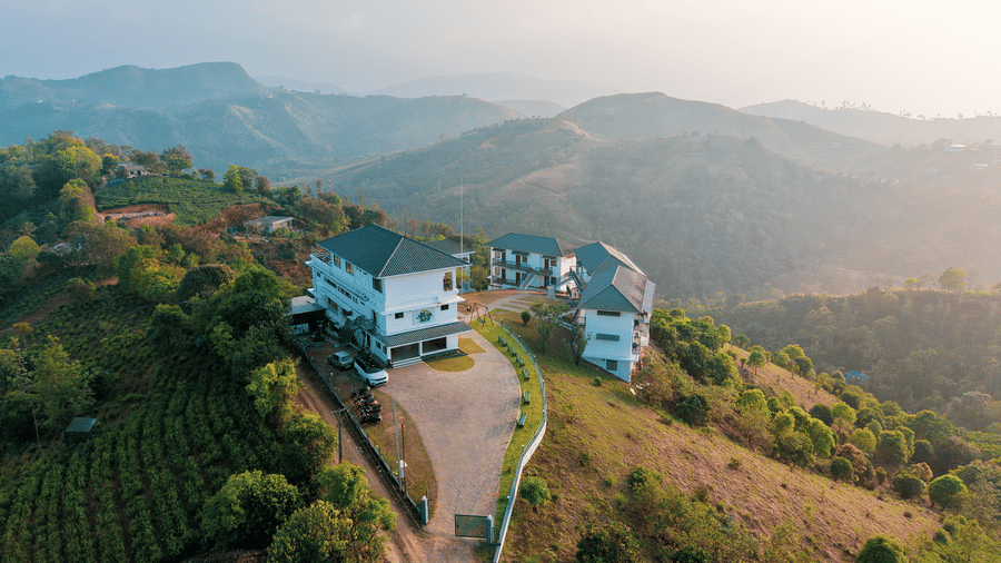 An aerial view of Abad Silvermist, Vagamon, the best family resorts in Vagamon, on a grassy hilltop surrounded by tea plantations and rolling mountains