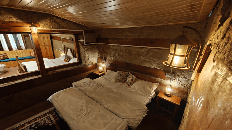An overhead shot of the double bed at the Friendship Peak Cottage with a wooden ceiling at Amara Upepo - The Sky Village, Manali.
