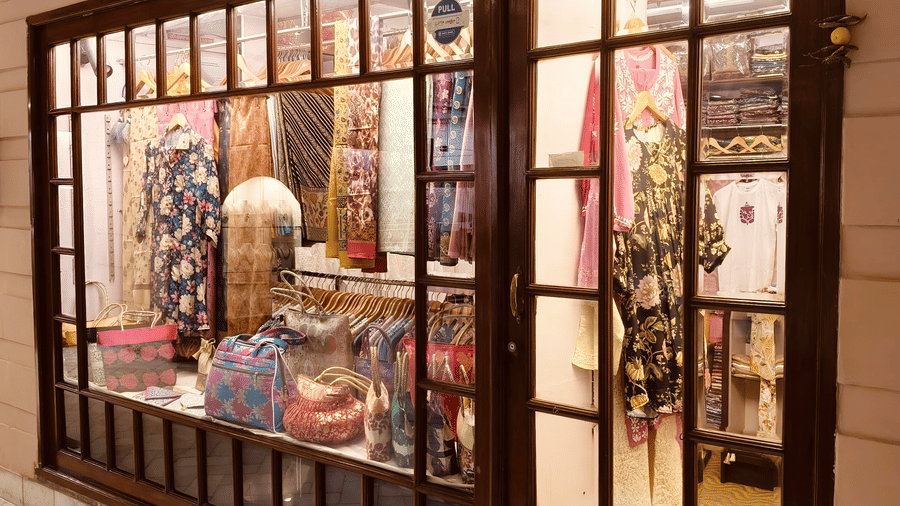 1000071313.jpgA shop window displaying patterned dresses, bags, and scarves on hangers and shelves | HHI Varanasi