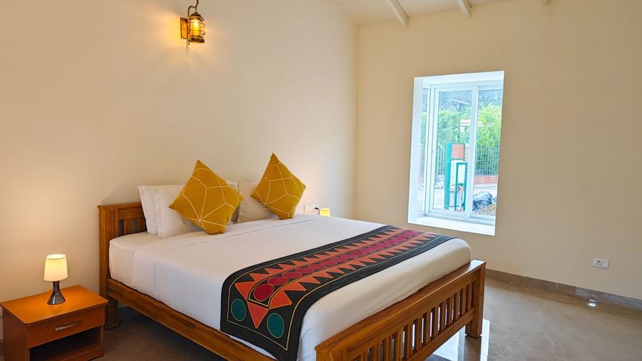 Bright bedroom with wooden double bed, yellow cushions, and bedside lamps at Ibex Resorts, Kotagiri.