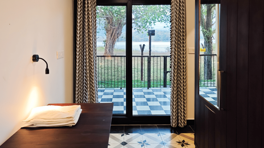 View from inside a guest room looking through glass sliding doors toward a tiled balcony and lush greenery - Ibex Resorts, Malampuzha (Kava Eco Camp and Caravan Park)