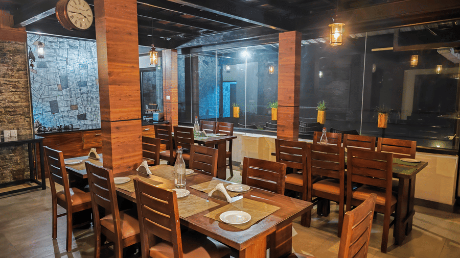 Well lit dining hall at Ibex Resorts Valparai Tale Rock showcasing handcrafted wooden tables brick pillars and ambient lighting providing guests with a warm and welcoming setting amidst the scenic surroundings of Valparai.