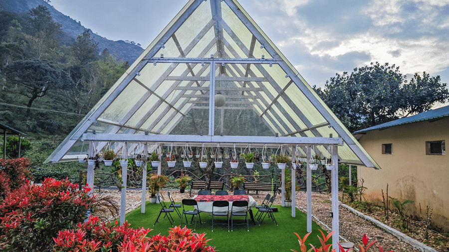 An outdoor space with a glass roof, comfortable seating underneath and a forest in the background at Ibex Resort, the best resort in Valparai.