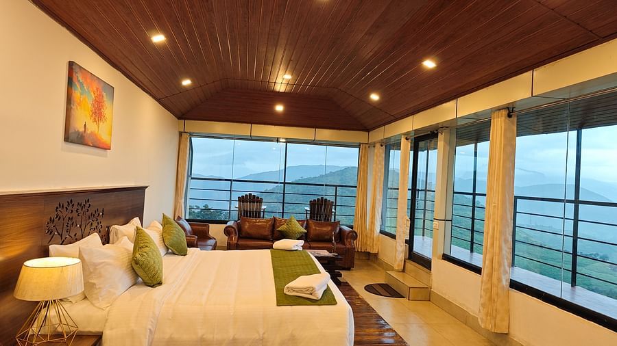 A side angle shot of the suite at the resort under yellow lights featuring a expansive balcony that overlooks the lush green valleys, king size bed with white bed sheets and a green bed runner  | Ibex Stays and Trails