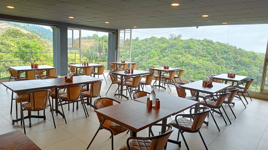 Open-air dining area with wooden tables and scenic hill views at The Cliff Edge Coorg Hotel.