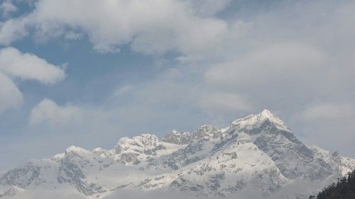 Snow-dusted mountain peaks emerging from fluffy clouds against a blue sky