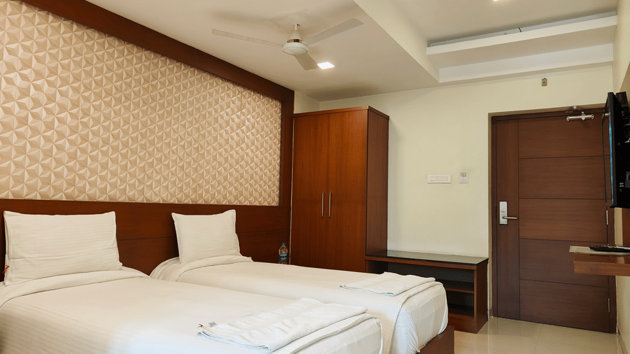 A room featuring twin beds with white linens, a textured tan headboard, and a dark wooden wardrobe and door | A & M Rooms and Residences