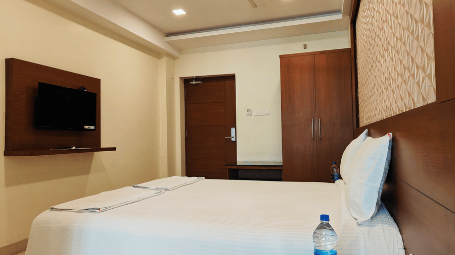 A well-furnished room, featuring a large bed with a padded headboard, a wall-mounted TV, and dark wood furnishings | A & M Rooms and Residences