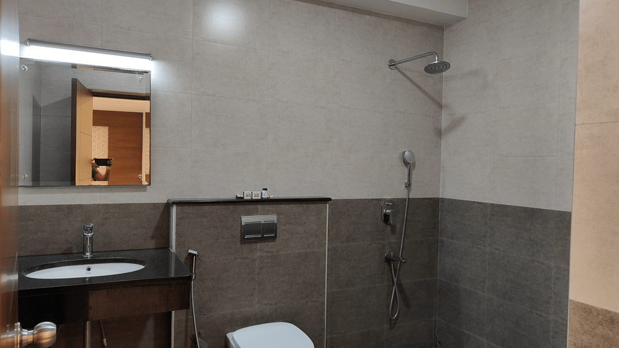 A bathroom with grey wall tiles, a dark wood vanity with a sink, a toilet, and a shower area | A & M Rooms and Residences