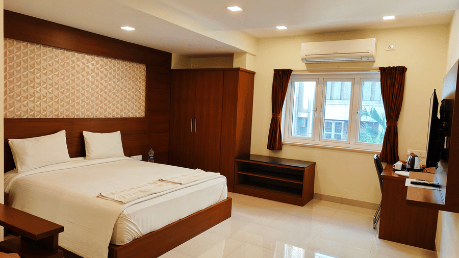 A spacious room featuring a large bed, dark wood panelling, a wall-mounted TV, and large windows with natural light | A & M Rooms and Residences