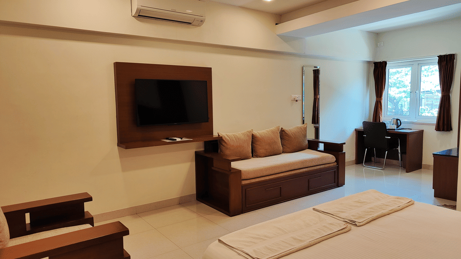 A room featuring a neatly made bed, a wall-mounted TV, and a sofa seating area | A & M Rooms and Residences