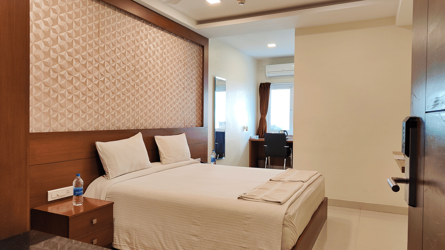 A wide-angle view of Deluxe King Room featuring a large bed with white linens, dark wood accents, and a mirror next to the bed at A & M Rooms and Residences.