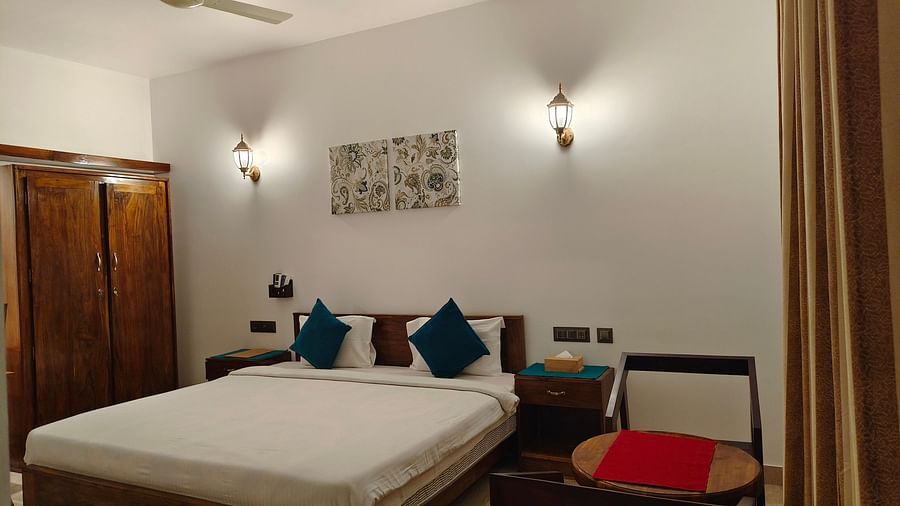 Another angle of a double bed with blue pillows, two chairs facing each other and a frame on the wall in102 room at Ananda Holiday Home, Wayanad 5