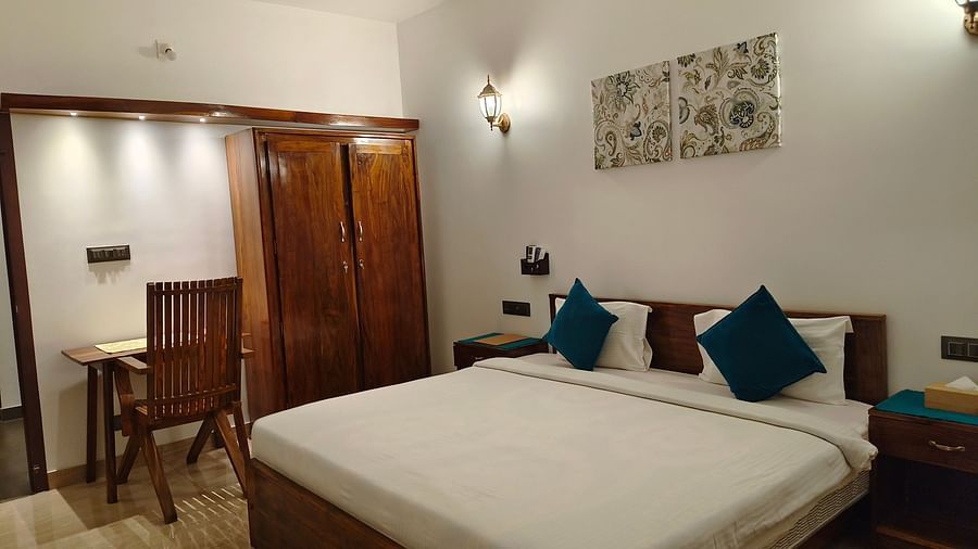 Wide view of a double bed with blue pillows, a chair and a cupboard in 102 room at Ananda Holiday Home, Wayanad 9