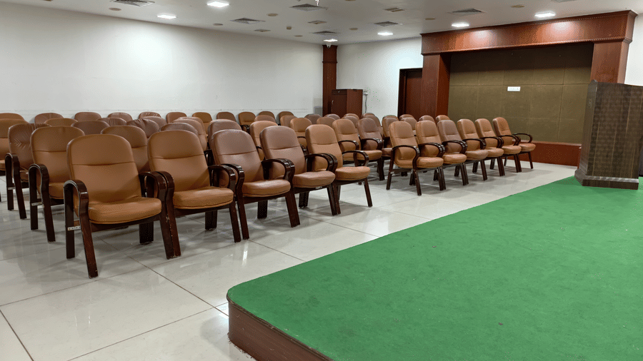 A conference room featuring rows of brown chairs, wooden podium, and raised green stage at DSF Grand Plaza, Tuticorin.