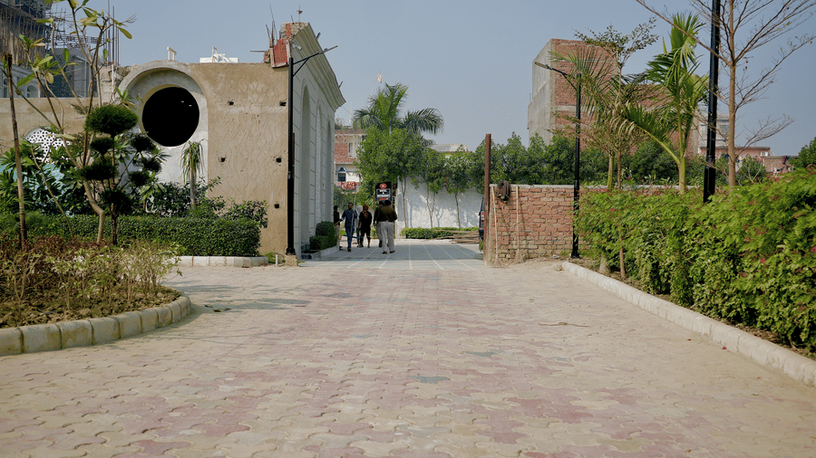 A paved walkway leading past a modern building with a circular window and lush green shrubs.