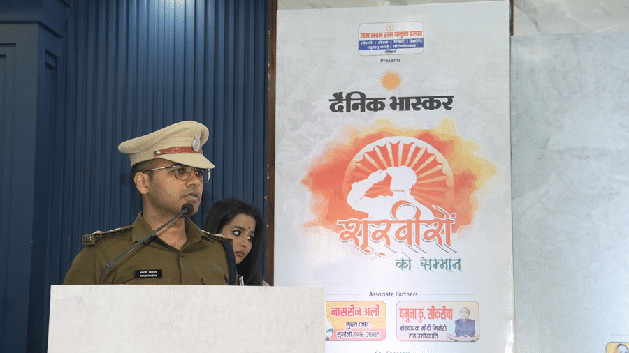 A police officer in uniform speaking at a podium in front of an event banner at the Ram Bhawan Ram Yamuna Prasad Hotel and Resort.