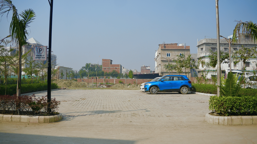 A wide outdoor parking area featuring a blue car parked near a low stone border and palm trees.