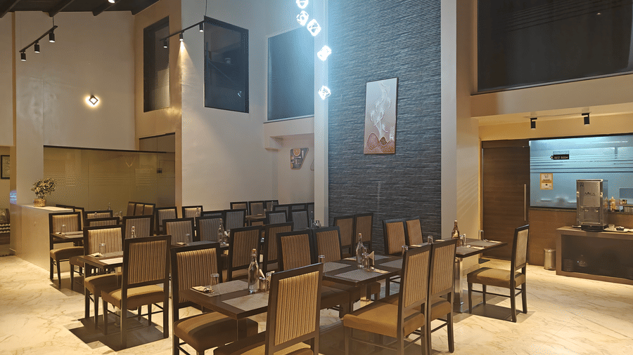 Modern restaurant dining area with neat rows of wooden tables and upholstered chairs, under warm ambient lighting at Trident The Boutique Hotel, Ooty.