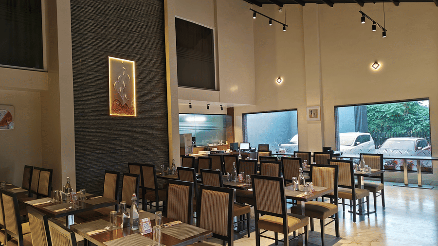 Wide-angle view of an elegant restaurant interior with a high ceiling, featuring several tables set for service at Trident The Boutique Hotel, Ooty.