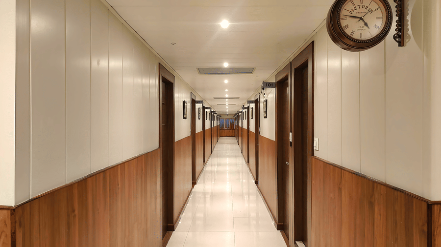 Corridor at Valmere Thistle Boutique Hotel, Darjeeling with wood-paneled walls, numbered guest room doors, and a Victoria Station-style wall clock.