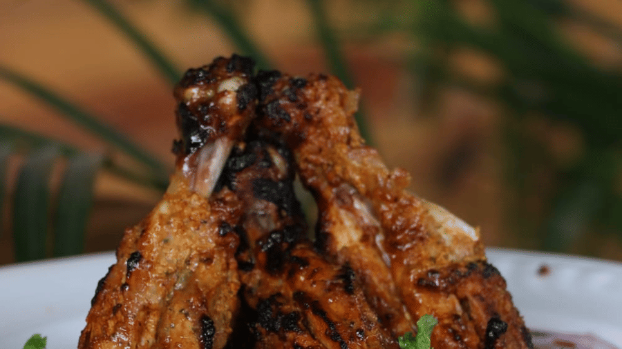Juicy tandoori chicken legs arranged on a plate over sliced onions with a sauce being poured on top, showcasing flavourful presentation at Papaya Tree Hotels.