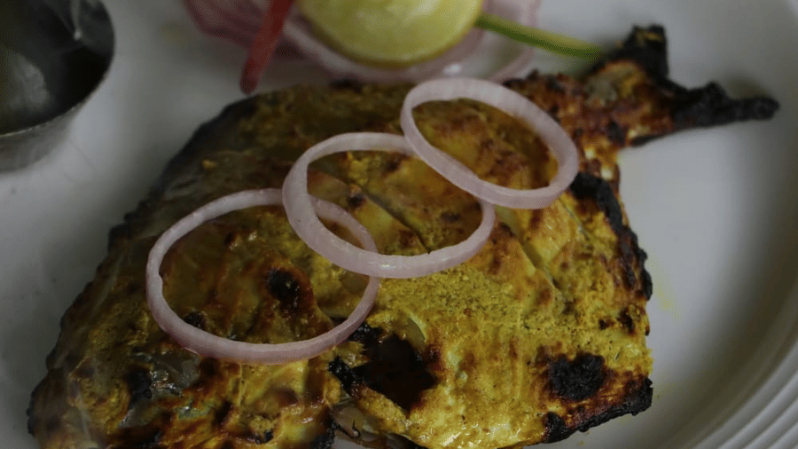 A dish featuring grilled chicken topped with onion rings, accompanied by mint chutney and salad, beautifully presented at Papaya Tree Hotels.