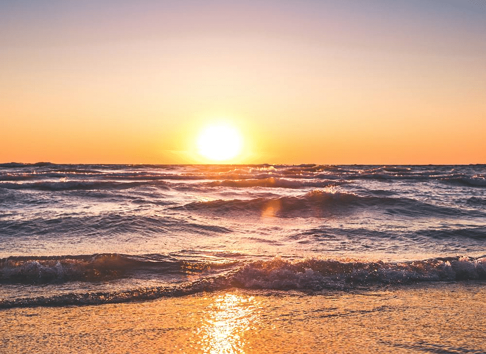  A breathtaking sunset over the ocean, with the sun casting a golden glow on the water and waves rolling onto the sandy shore.