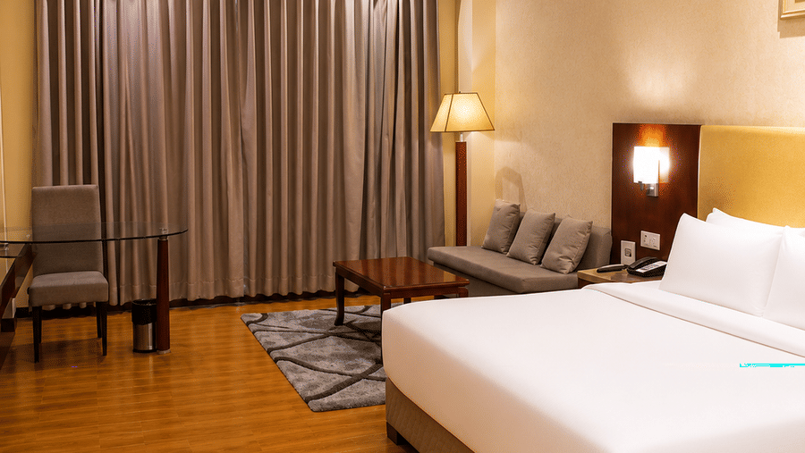 Deluxe room at Golden Tulip Kukas Jaipur with a king bed, bedside chair, framed wall art, dark curtains, and warm ambient ceiling lighting