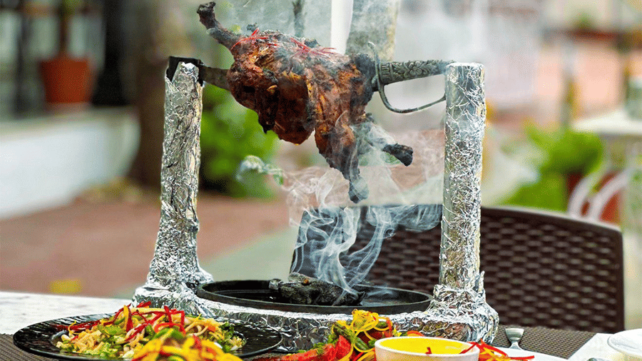 An outdoor table at Amantra Shilpi Resort, Udaipur, set with plates of noodles and a vertical skewer of roasted meat.