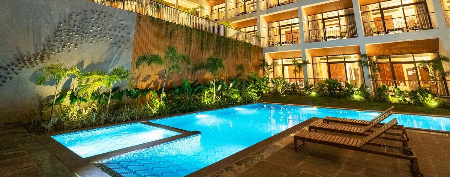 An exterior night view of a luxurious hotel building with a brightly lit swimming pool and lush landscaping. - Sea Hills Resort, Swaraj Dweep (Havelock)