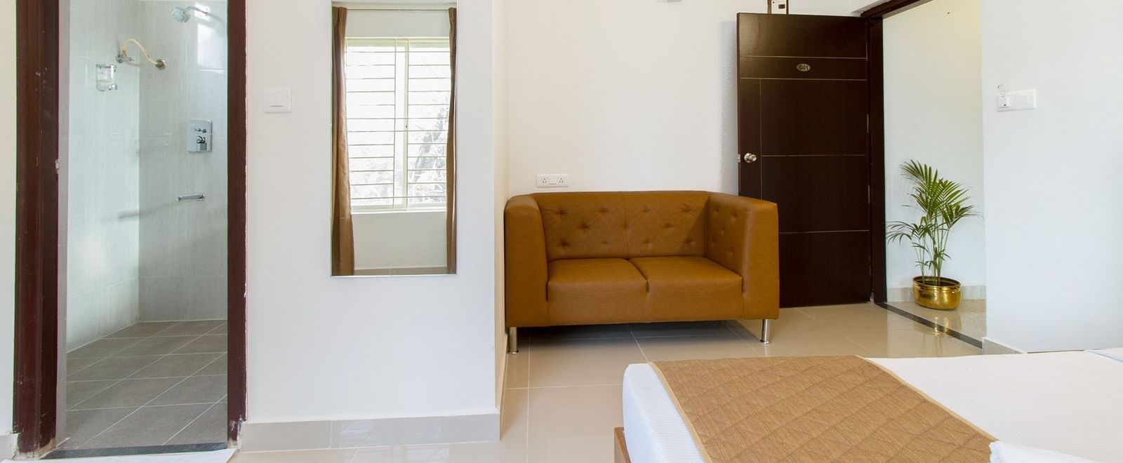 A room with a full-length mirror, an armchair, and a doorway leading to the washroom at Sanctum Suites Whitefield, Bangalore.