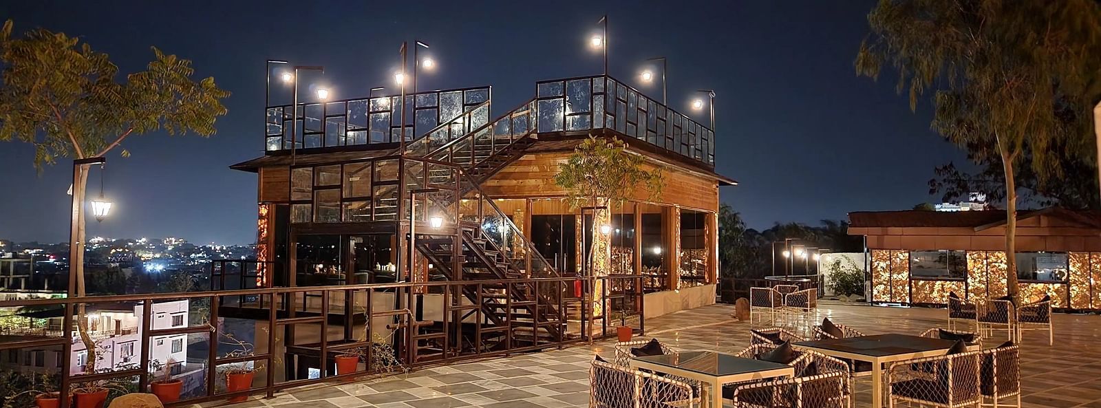Outdoor restaurant at night, lit building, tables, and trees.