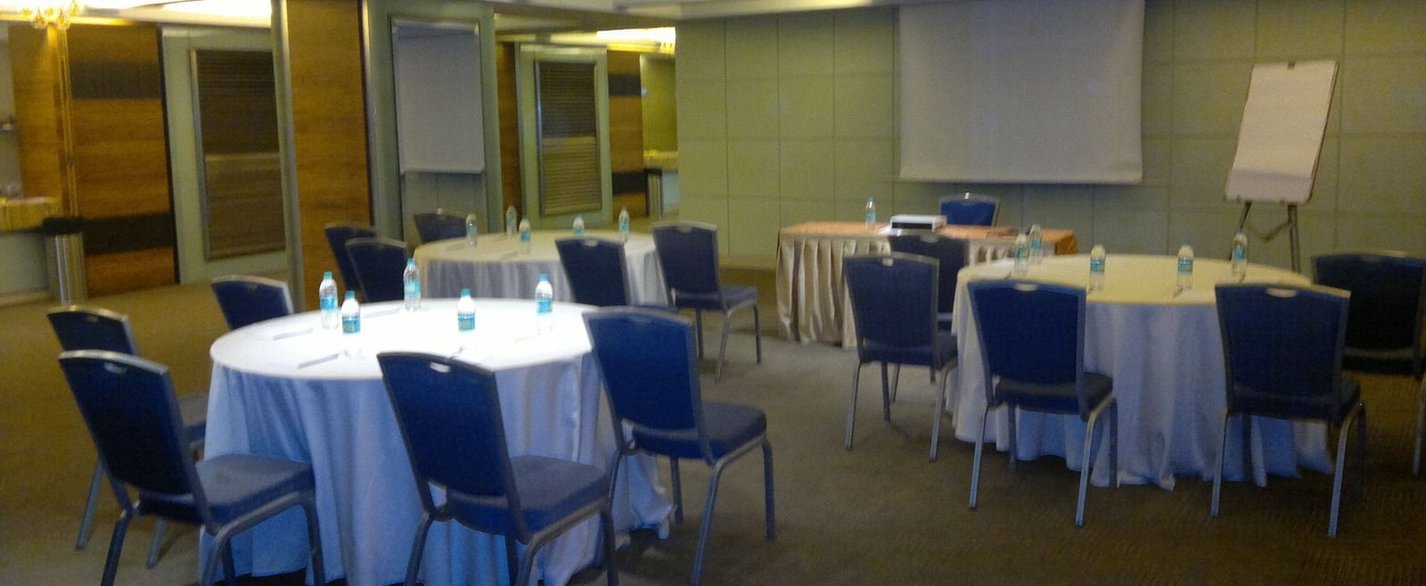 Image of an event space at Mirage Hotel featuring round tables and blue chairs along with a white board | Mirage Hotel