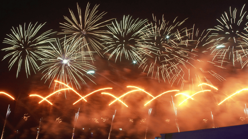 A night-time view of a fireworks display with golden trails and bursts above a dark silhouette.