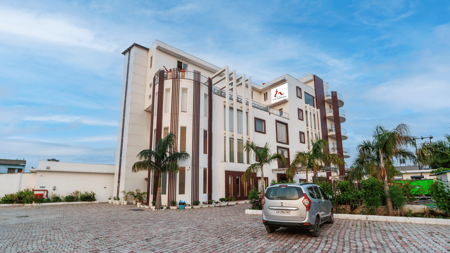 Exterior view of Inde Reva Resorts Rishhikesh with paved driveway, parked car and palm trees.